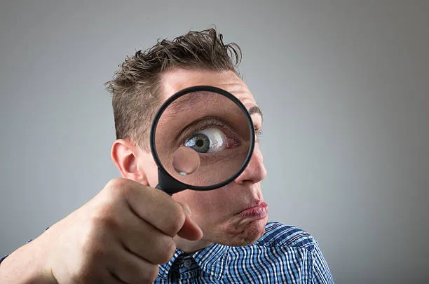 A screenshot of a man holding a magnifying glass.